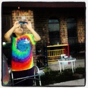 Noemi's daughter using a camera, her walker in front of her. She is wearing a tie-die shirt.