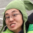 An woman smiling, wearing glasses and a green knit Yoda hat