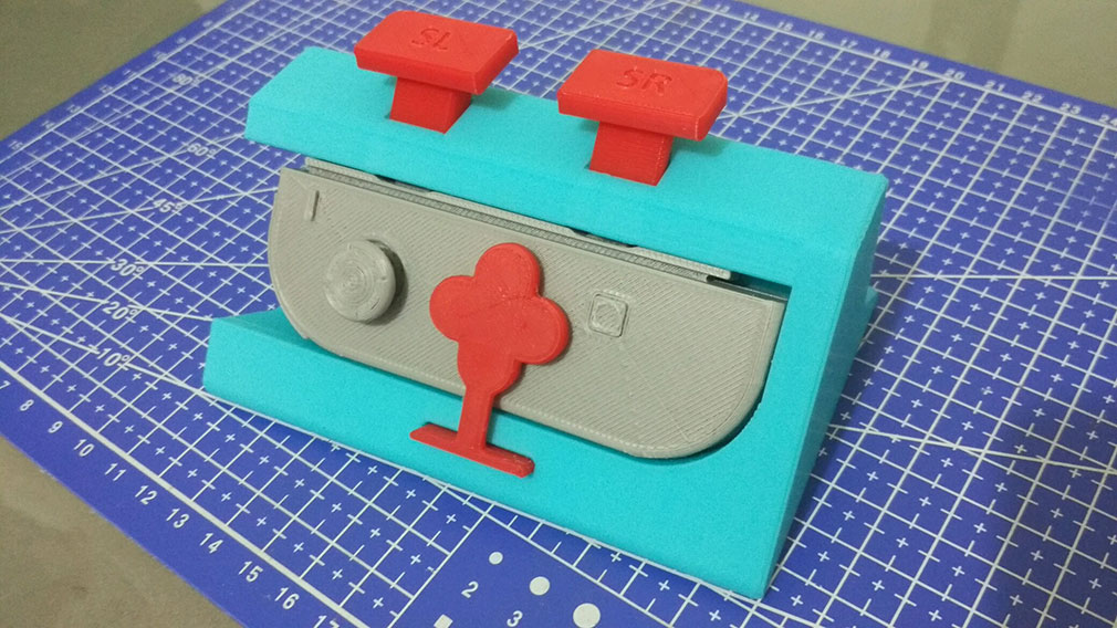A blue 3D printed case surrounding a printed, gray controller. There are two red buttons on top for the left and right controls.