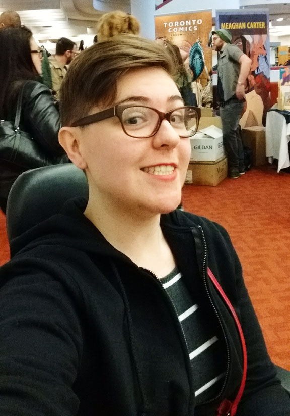Woman with short hair and glasses sitting in a scooter at a convention hall