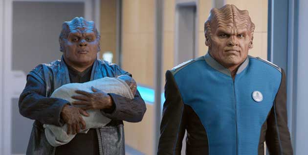 Bortus and his partner walking down a hallway, a baby in his arms. They look like Klingons