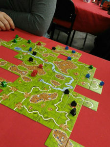 Carcassone game on a table, the green, square tiles laid out with meeples on the roadways